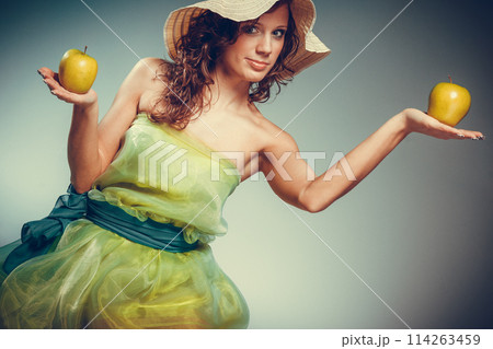 Woman in dress and hat hold yellow apple 114263459