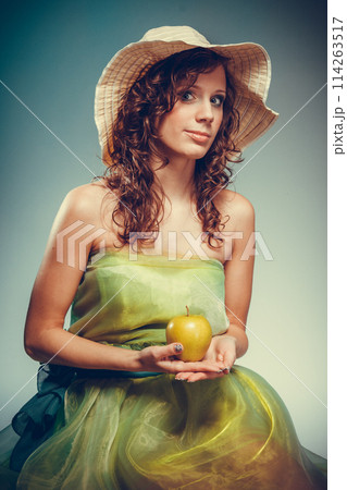 Woman in dress and hat holding yellow apple. 114263517