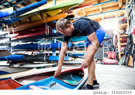 Young canoeist preparing canoe and paddle, going on water. Concept of canoeing as dynamic and adventurous sport. Young canoeist preparing canoe and paddle, going on water. Concept of canoeing as dynamic and adventurous sport. 114263554