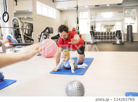 Father smiling at baby while performing exercise above. Group exercise class, fitness or pilates for parents. Parents staying active while boding with babies. Father smiling at baby while performing exercise above. Group exercise class, fitness or pilates for parents. Parents staying active while boding with babies. 114263769