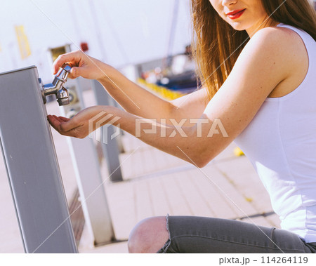 Woman drinking water from tap in marina. 114264119
