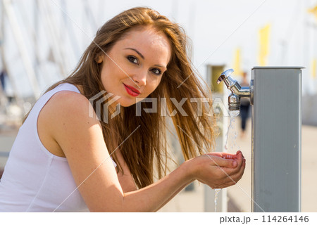 Woman drinking water from tap in marina. 114264146