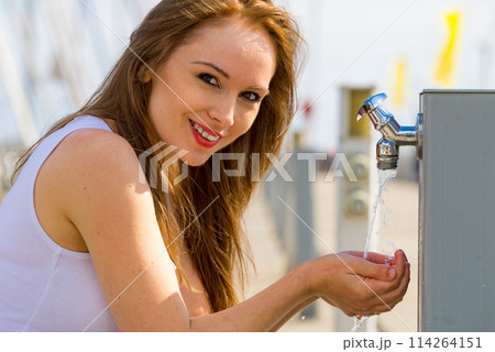 Woman drinking water from tap in marina. 114264151