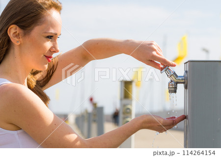 Woman drinking water from tap in marina. 114264154