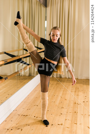 Young woman ballerina stretching and training at barre in dance studio - ballet and dancer concept 114264424
