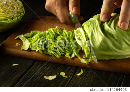 Male hands using a knife cut fresh cabbage on a kitchen board to prepare a vegetable salad at home for lunch 114264498
