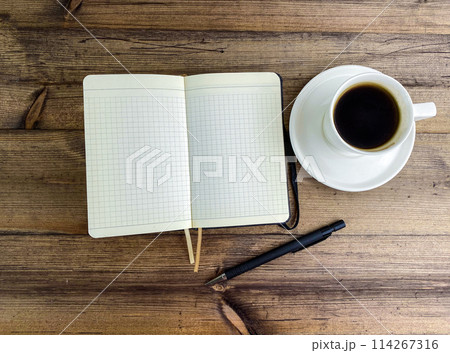 Coffee in a cup and a notebook with a pen on the table, top view. 114267316