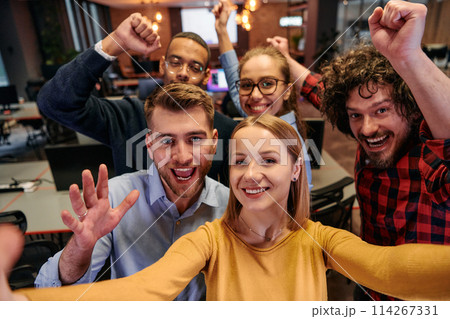 A diverse group of business professionals take a break from their tasks in a modern startup office to capture a creative selfie, showcasing teamwork and a vibrant workplace culture 114267331