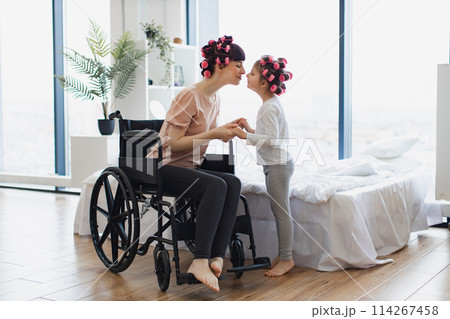 Young mother in wheelchair holds hands of her little daughter on weekend. Young mother in wheelchair holds hands of her little daughter on weekend. 114267458