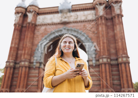 Woman with smart phone in summer vacation travel, standing near Barcelona triumphal arch. Female traveler visiting local landmarks. Concept of travel, tourism and vacation in city Woman with smart phone in summer vacation travel, standing near Barcelona triumphal arch. Female traveler visiting local landmarks. Concept of travel, tourism and vacation in city 114267571