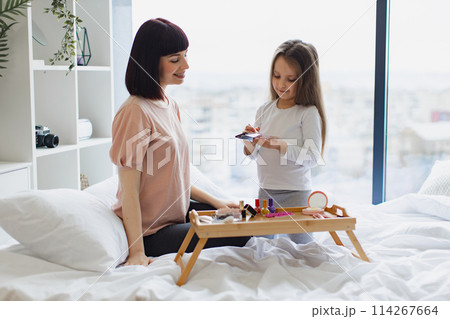 Portrait of Caucasian daughter applying powder on her young mom's face. 114267664