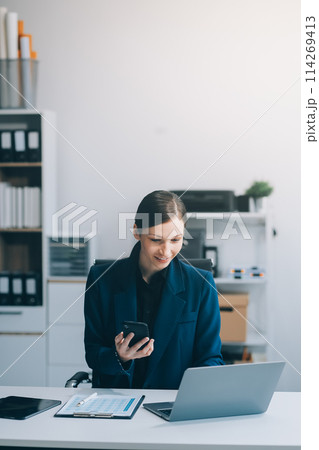 Asian businesswoman holding mobile phone with laptop looking at information laughing at news for online shopping happy. Asian businesswoman holding mobile phone with laptop looking at information laughing at news for online shopping happy. 114269413