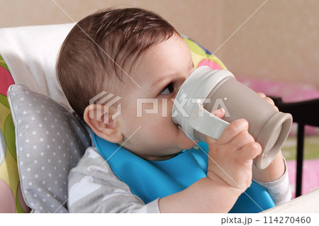Handsome serious sweet little boy child sitting at table drink water baby from bottle, closeup Handsome serious sweet little boy child sitting at table drink water baby from bottle, closeup 114270460