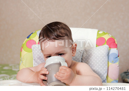Handsome serious sweet little boy child sitting at table drink water baby from bottle, closeup 114270481