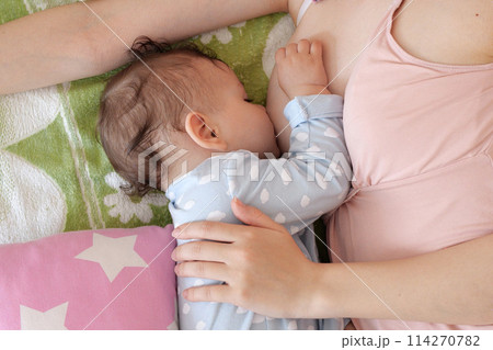 Young woman breastfeeding her baby at home. Milk from mother's breast is a natural medicine to baby. Mother day bonding concept with newborn baby nursing Young woman breastfeeding her baby at home. Milk from mother's breast is a natural medicine to baby. Mother day bonding concept with newborn baby nursing 114270782