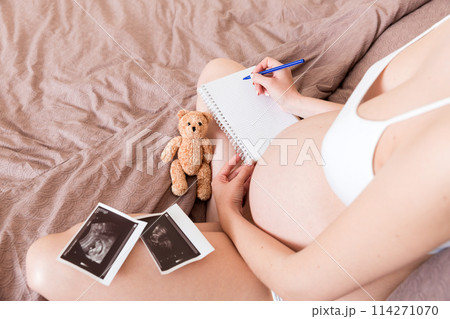 Top view caring future mother writing diary with ultrasound. pregnant woman tummy making notes feeling during pregnancy or creating scrapbook Top view caring future mother writing diary with ultrasound. pregnant woman tummy making notes feeling during pregnancy or creating scrapbook 114271070