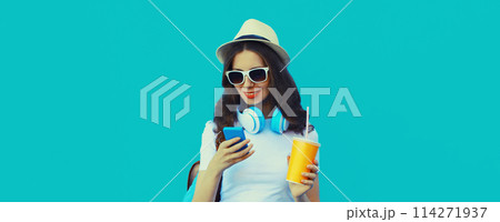 Portrait of modern young woman listening to music with headphones holding phone on blue background 114271937