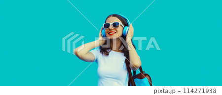 Happy modern happy young woman listening to music with headphones on blue background 114271938