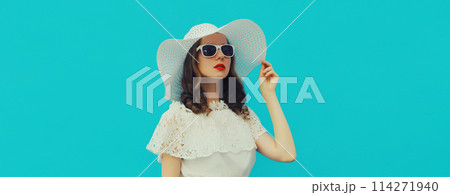 Beautiful caucasian young woman model posing wearing white summer straw hat on blue background Beautiful caucasian young woman model posing wearing white summer straw hat on blue background 114271940