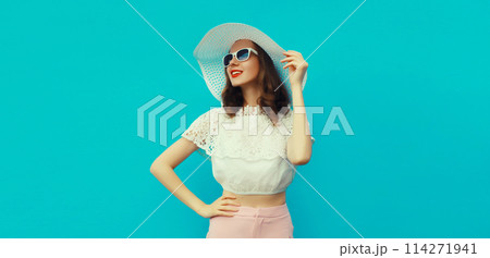 Beautiful caucasian young woman model posing wearing white summer straw hat on blue background Beautiful caucasian young woman model posing wearing white summer straw hat on blue background 114271941