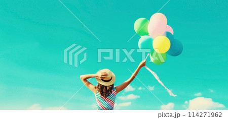 Happy joyful woman with bunch of colorful balloons in summer straw hat on blue sky background 114271962