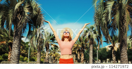 Summer vacation, happy cheerful young woman raising her hands up on palm tree background Summer vacation, happy cheerful young woman raising her hands up on palm tree background 114271972