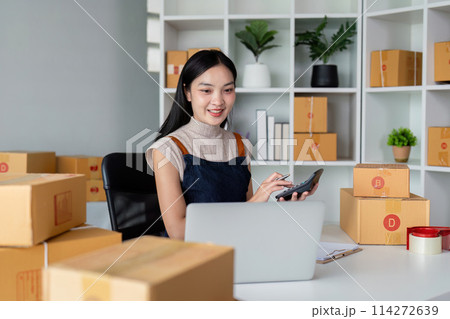 Young business woman asian working online ecommerce shopping at her shop. Young woman sell prepare parcel box of product for deliver to customer. Online selling Young business woman asian working online ecommerce shopping at her shop. Young woman sell prepare parcel box of product for deliver to customer. Online selling 114272639