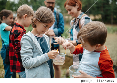 Young students analyzing water quality, ph level with indicator strips during biology field teaching class. Female teacher during outdoor active education. Young students analyzing water quality, ph level with indicator strips during biology field teaching class. Female teacher during outdoor active education. 114273633
