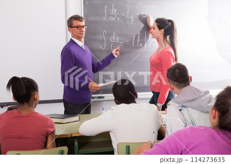 Schoolgirl solves task near blackboard in classroom mathematics Schoolgirl solves task near blackboard in classroom mathematics 114273635