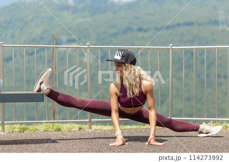 Athletic woman doing single leg split squat exercise with park equipment outdoors high buildings in background Athletic woman doing single leg split squat exercise with park equipment outdoors high buildings in background 114273992