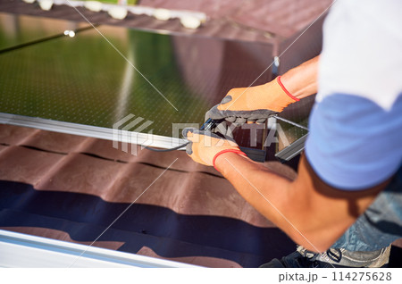 Worker installing solar panel system on roof of house. Close up electrician connecting modules together for generating electricity through photovoltaic effect. Concept of alternative, renewable energy Worker installing solar panel system on roof of house. Close up electrician connecting modules together for generating electricity through photovoltaic effect. Concept of alternative, renewable energy 114275628