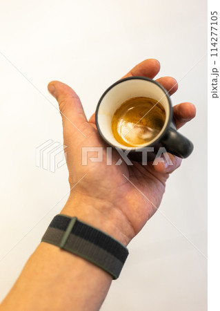 Hand holding a freshly brewed espresso in a black cup 114277105