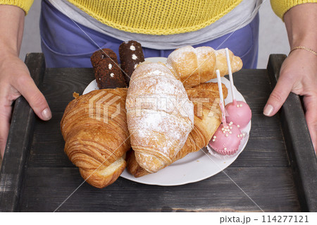 Hands hold a tray with sweets and pastries. 114277121