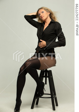 Beautiful elderly woman in black stockings posing in the studio on a gray background. 114277799
