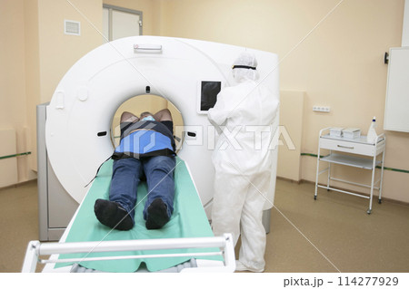 Doctors in protective medical suits are doing an MRI scan to a patient with coronavirus infection. 114277929