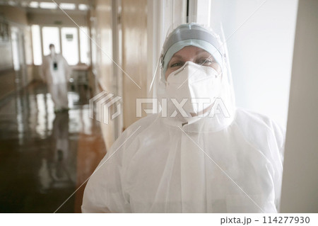 A doctor in a protective medical suit stands on the corridor of the hospital and smiles. 114277930