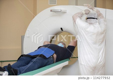 Doctors in protective medical suits are doing an MRI scan to a patient with coronavirus infection. 114277932