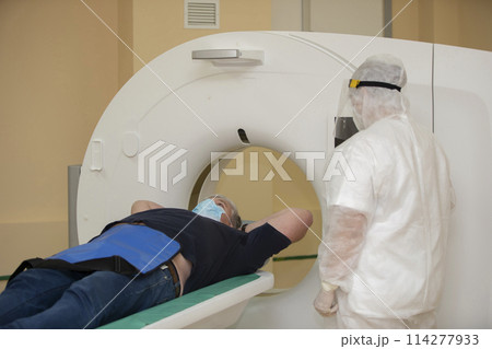 Doctors in protective medical suits are doing an MRI scan to a patient with coronavirus infection. 114277933