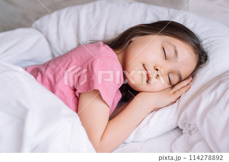 Little girl in pink pajamas sleeps in a white bed 114278892