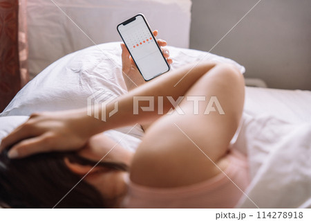 The girl has stomach pain and lies in bed holding a phone with a calendar in her hand 114278918