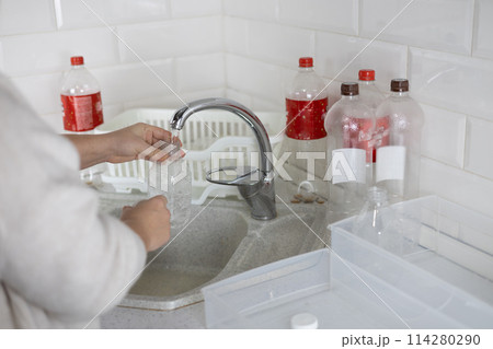 Sorting plastic in the kitchen, a woman washes bottles and puts them in a box. A woman puts plastic waste into boxes for recycling. The concept of protecting the planet from plastic pollution. Sorting plastic in the kitchen, a woman washes bottles and puts them in a box. A woman puts plastic waste into boxes for recycling. The concept of protecting the planet from plastic pollution. 114280290