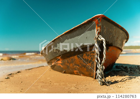 Old fishing boat rusting on sandy shore under sunny skies 114280763