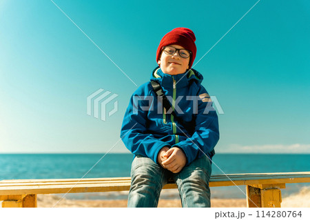 A boy is sitting on a bench on a spring beac 114280764