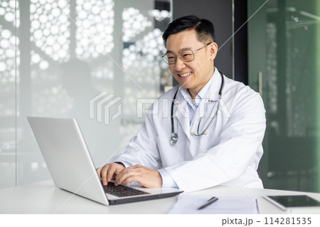 A cheerful mature Asian male doctor in a white coat and glasses, working on a laptop in a modern office, radiating positivity and professionalism. A cheerful mature Asian male doctor in a white coat and glasses, working on a laptop in a modern office, radiating positivity and professionalism. 114281535