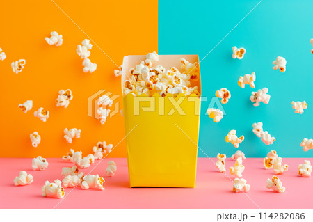 A red and white striped popcorn bucket full of fluffy, buttery popcorn, bold colors of background 114282086