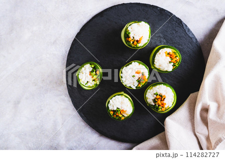 Close up of vegetable sushi made of rice, cucumber and carrots on a slate board top view Close up of vegetable sushi made of rice, cucumber and carrots on a slate board top view 114282727