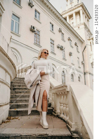 A woman wearing a white shirt and a tan coat is walking up a set of stairs. She is carrying a handbag and she is in a hurry. Concept of urgency and movement. 114283520
