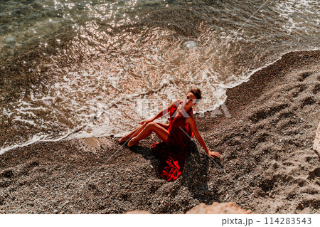 Woman red dress sea. Female dancer in a long red dress posing on a beach with rocks on sunny day 114283543
