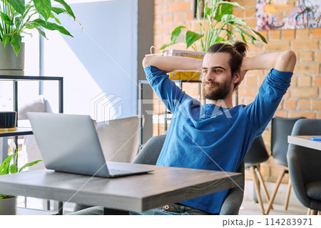 Satisfied relaxed young man looking at laptop screen while sitting in coworking cafe Satisfied relaxed young man looking at laptop screen while sitting in coworking cafe 114283971