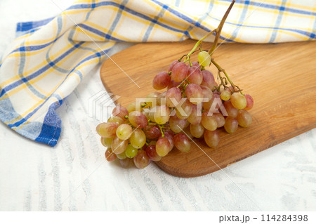 Cutting board with bunch of organic pink grapes on white wooden background.. Cutting board with bunch of organic pink grapes on white wooden background.. 114284398